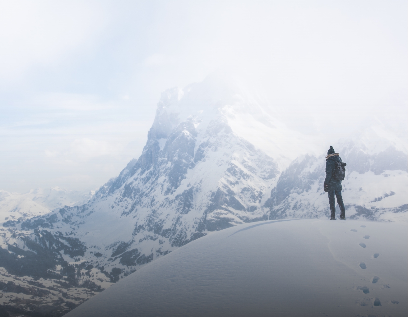 This is an image that shows a snowy mountain with a person standing in front of it